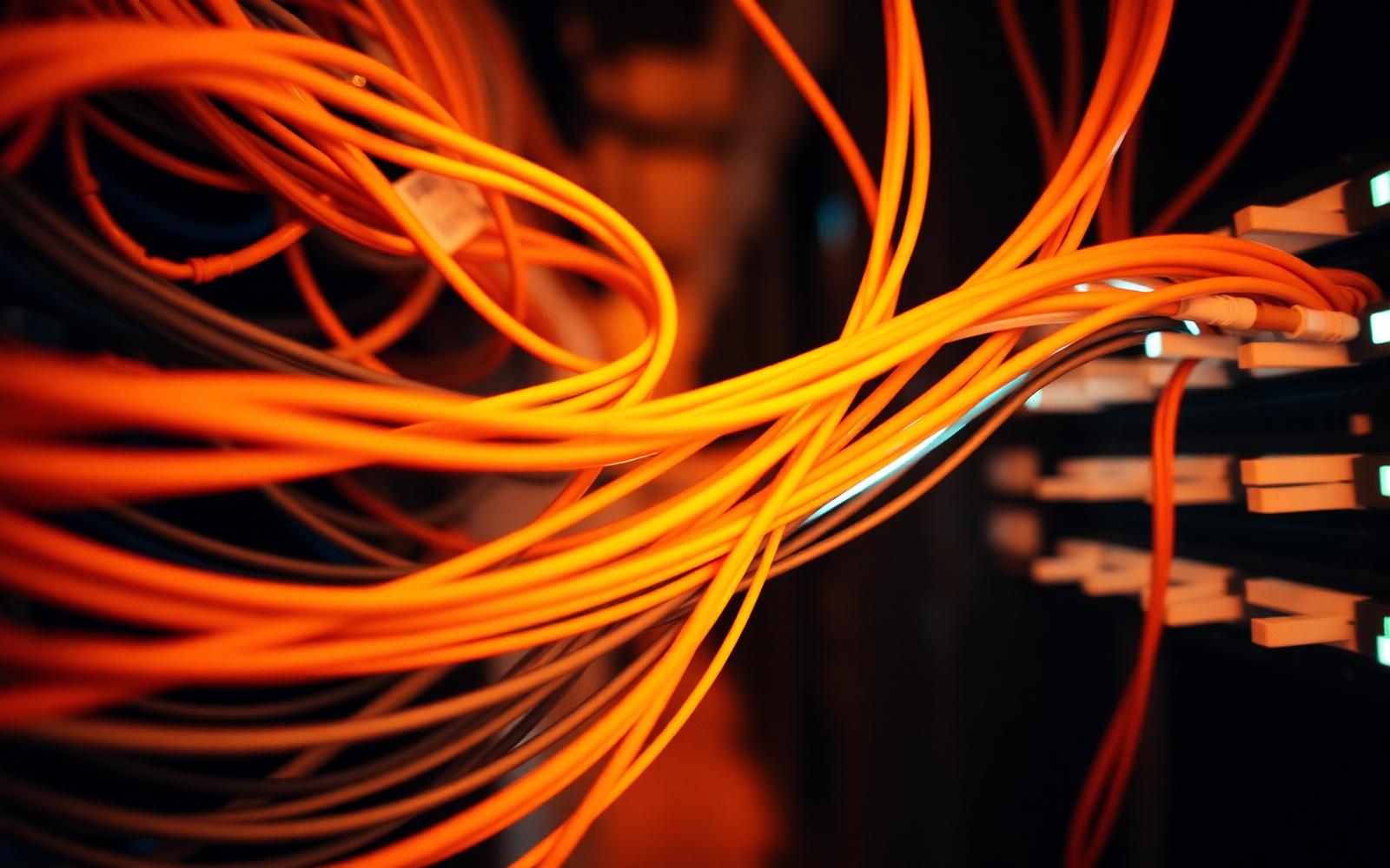 Warm amber fibre-optic cabling passing through a network patch panel